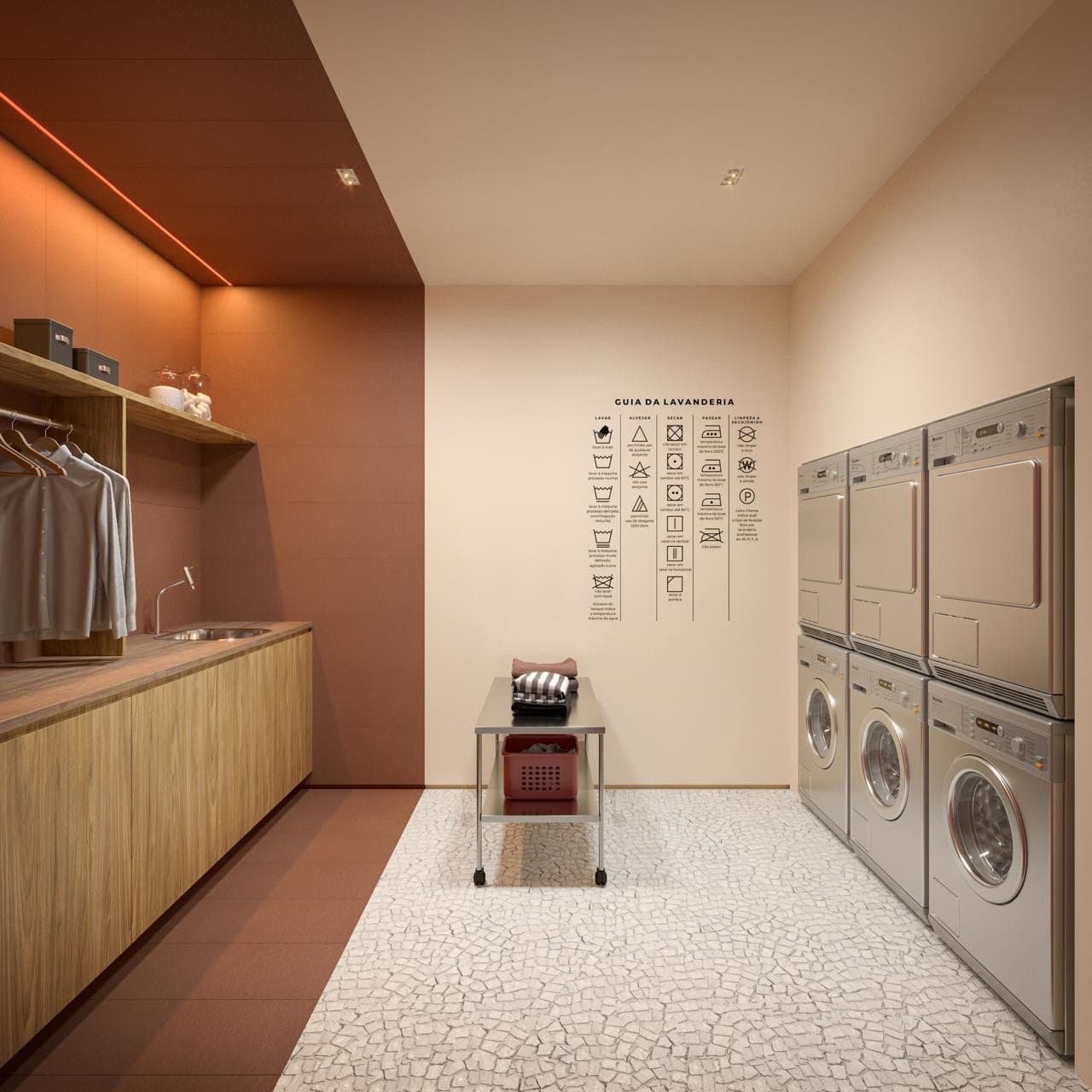 Lavanderia compartilhada do Garcya Praia Studios com máquinas de lavar e secar industriais, bancada com pia, cabideiro, guia ilustrado na parede e design moderno em tons terracota.