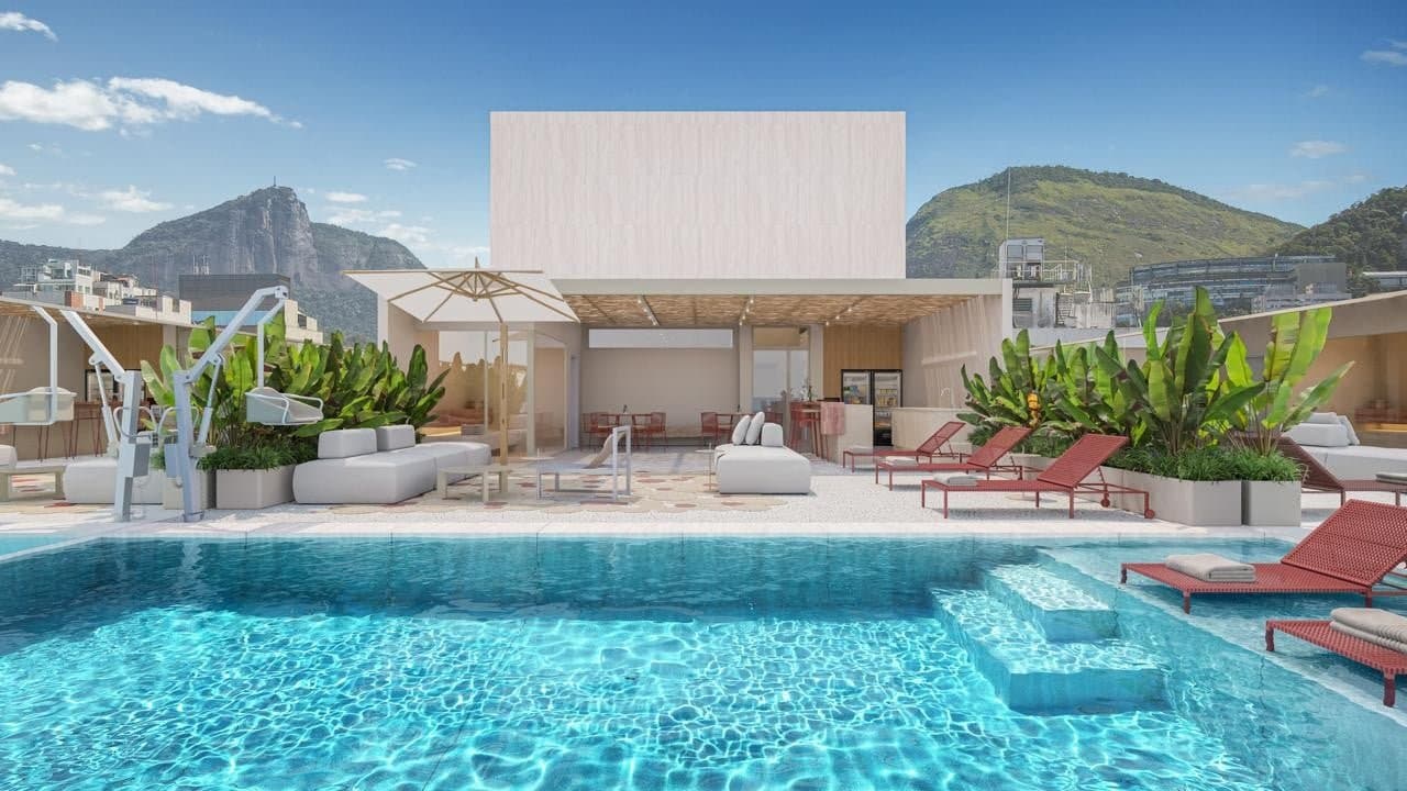 Área de lazer no rooftop do Garcya Praia Studios com piscina, espreguiçadeiras vermelhas, lounge com sofás, paisagismo com bananeiras e vista para o Cristo Redentor.